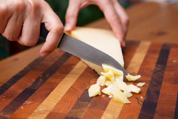 Mani femminili che tagliano parmigiano sul bordo di legno