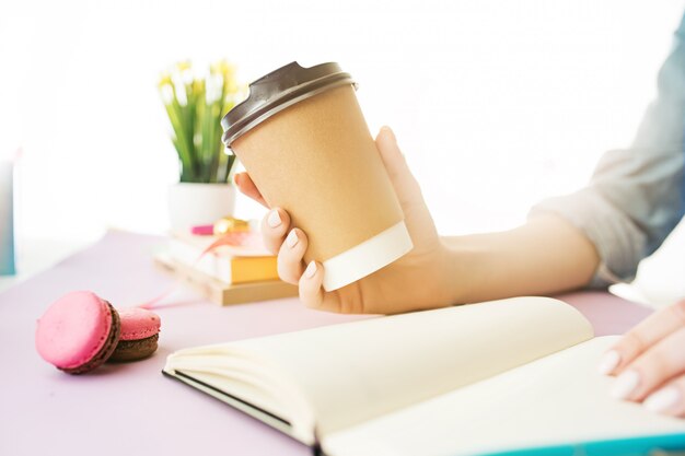 mani femminili che tengono caffè. scrivania rosa alla moda.