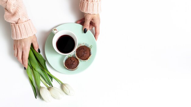 Mani femminili che tengono fiori e muffin con lo spazio della copia