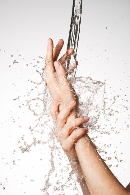 Mani femminili del primo piano sotto il flusso di spruzzi d'acqua - concetto di cura della pelle