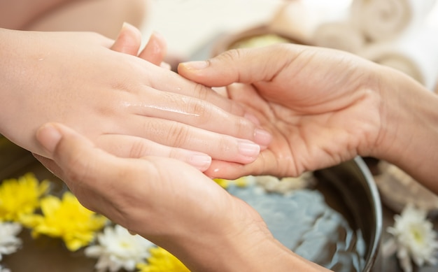 Mani femminili e ciotola di acqua termale con fiori, primi piani. Mani Spa.