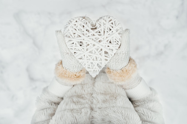 Mani femminili in guanti lavorati a maglia bianchi con un cuore bianco romantico d&#39;annata intrecciato