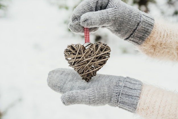 Mani femminili in guanti lavorati a maglia con un cuore romantico vintage intrecciato