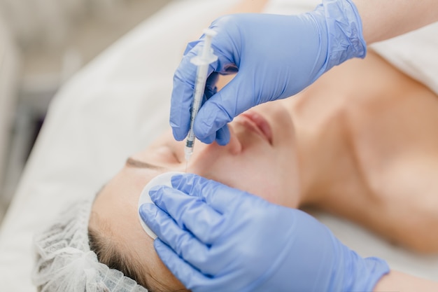 Mani in bagliori blu del cosmetologo al lavoro con bella donna durante l'iniezione sul viso. Ringiovanimento, professionista, sanità, medicina, terapia medica, cura della pelle, botox