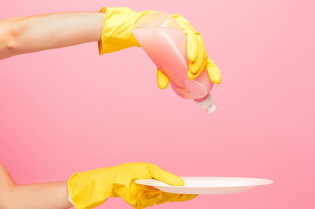 Mani in guanti protettivi gialli che lavano un piatto