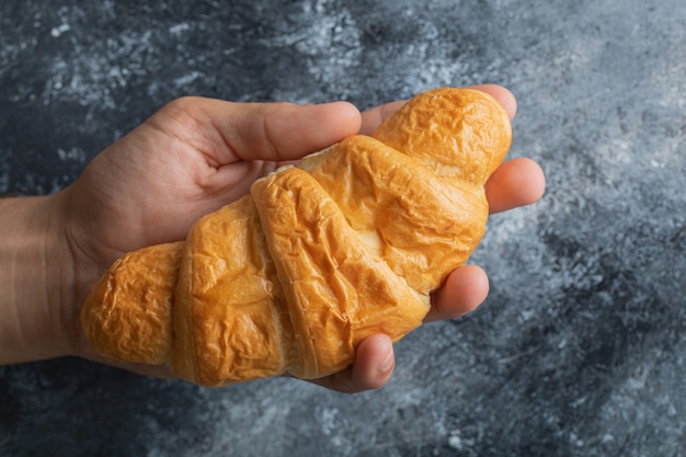 Mani maschili che tengono croissant fresco su sfondo di marmo