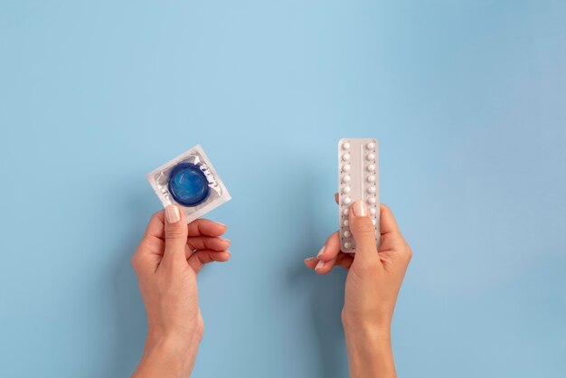 Mani ravvicinate che tengono preservativo e pillole