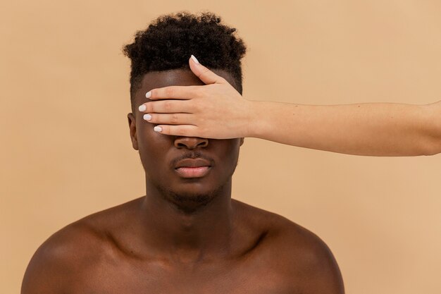 Mano bianca del primo piano che copre gli occhi dell'uomo di colore