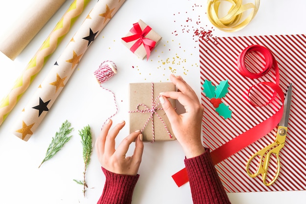 Mano che lega il contenitore di regalo dell&#39;arco sulla tabella bianca