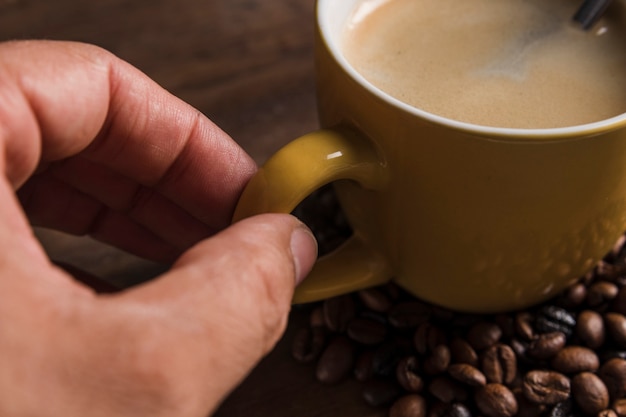 Mano che regge la maniglia della tazza con il caffè