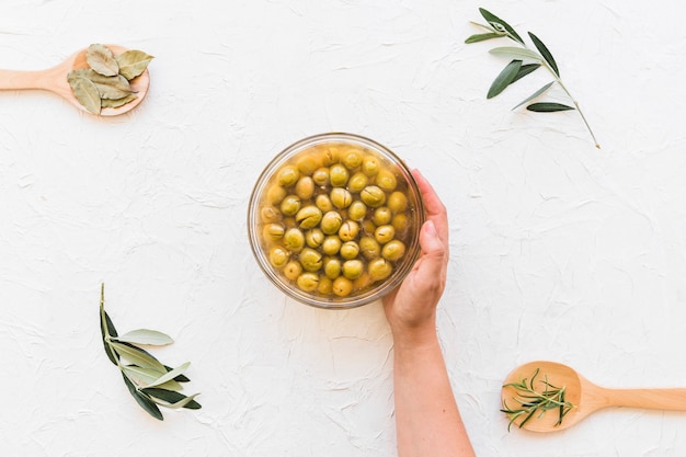 Mano che tiene ciotola di olive con erbe sul contesto in legno