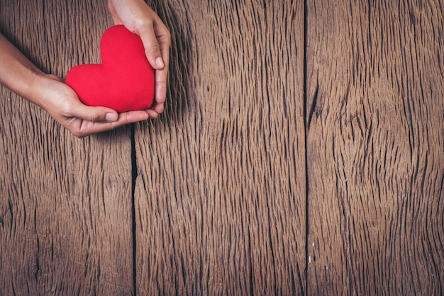 Mano che tiene cuore rosso su sfondo di legno