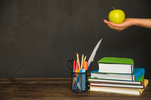 Mano che tiene la mela sul posto di lavoro con libri e articoli di cancelleria