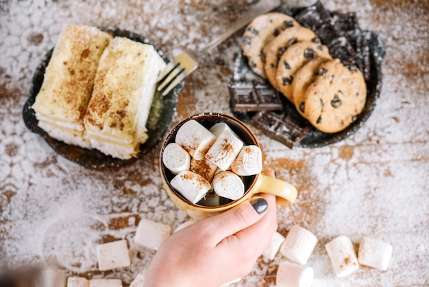 Mano che tiene tazza sul tavolo con dolci