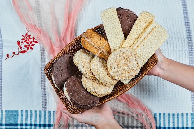 Mano che tiene un cesto di biscotti misti su una tovaglia.