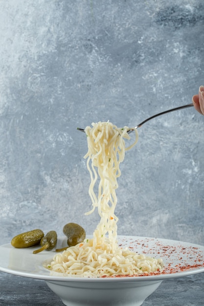 Mano che tiene un cucchiaio con tagliatelle e cetrioli sottaceto.