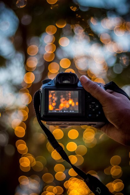 Mano che tiene una fotocamera digitale su uno sfondo di luci bokeh