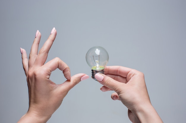 Mano che tiene una lampadina a incandescenza su sfondo grigio