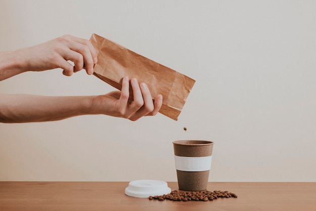 Mano che versa i chicchi di caffè da un sacchetto di carta in una tazza di caffè