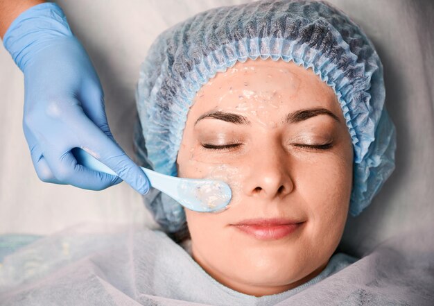 Mano cosmetologo che applica maschera cosmetica sul viso della donna