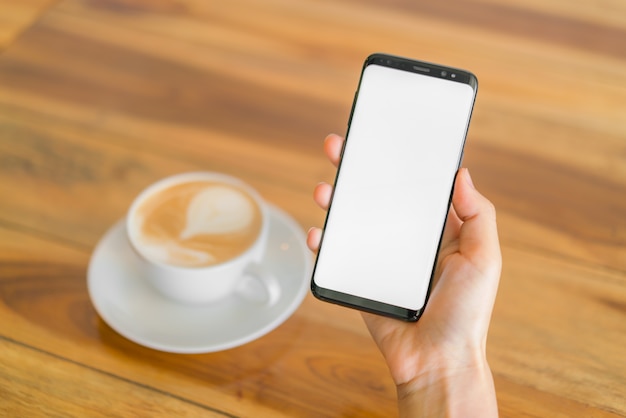 Mano d&#39;affari con il telefono cellulare e il latte art coffee.