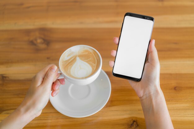 Mano d&#39;affari con il telefono cellulare e il latte art coffee.