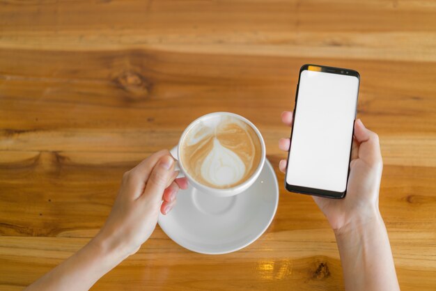 Mano d&#39;affari con il telefono cellulare e il latte art coffee.