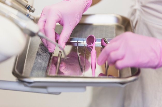 Mano del dentista in guanti rosa che sistemano gli strumenti dentari sul vassoio