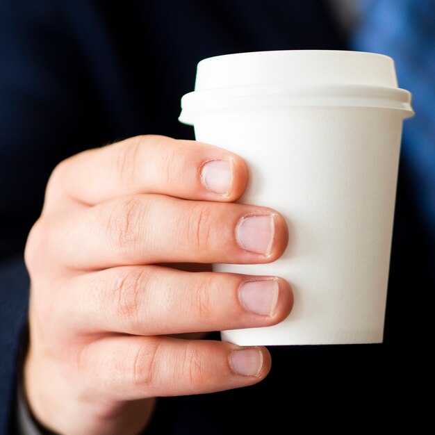 Mano del primo piano che tiene piccolo modello della tazza di caffè