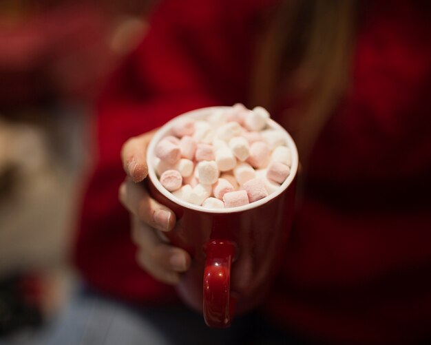 Mano del primo piano che tiene tazza con marshmallow