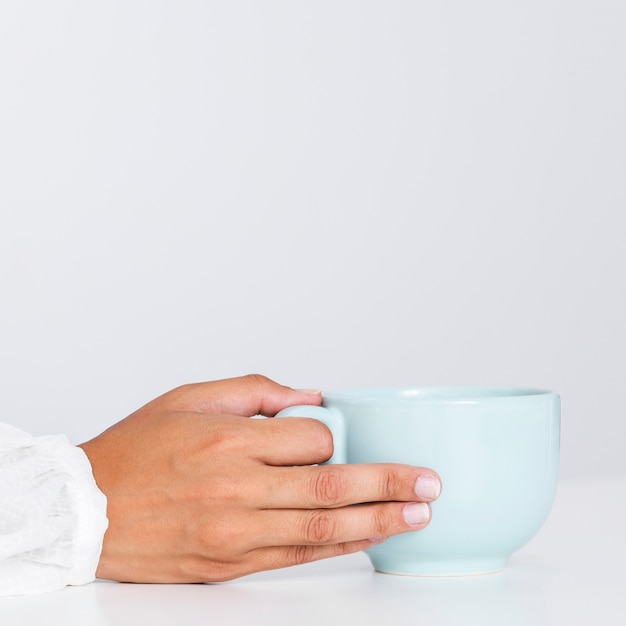 Mano del primo piano che tiene tazza di ceramica