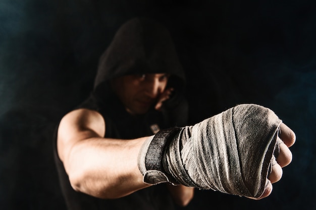 Mano del primo piano con la fasciatura del kickboxing di addestramento dell'uomo muscolare sul nero