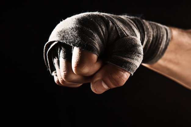 Mano del primo piano con la fasciatura del kickboxing di addestramento dell'uomo muscolare sul nero