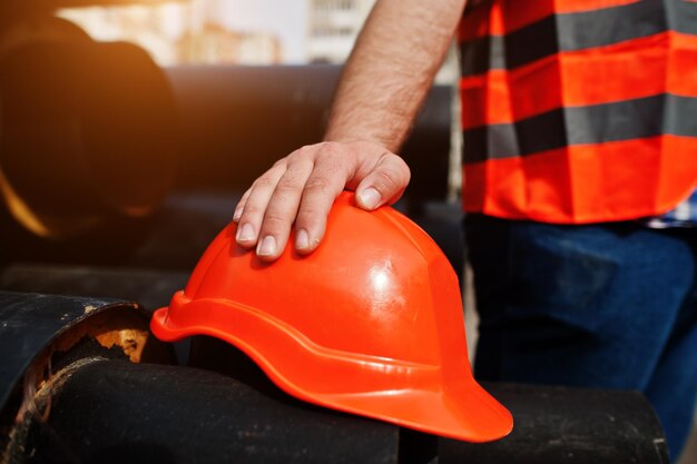 Mano dell'uomo del lavoratore in casco arancione di sicurezza vicino ai tubi d'acciaio