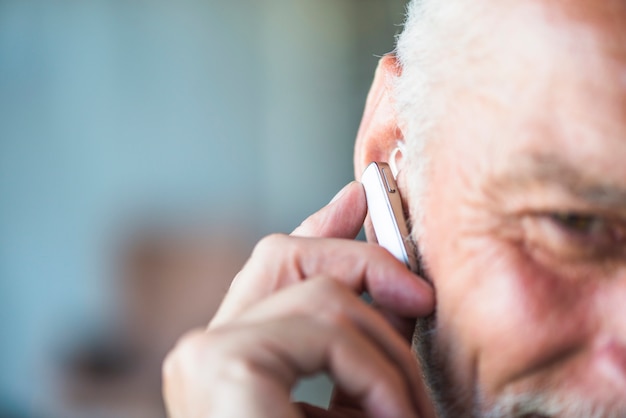 Mano dell&#39;uomo maggiore che mette l&#39;auricolare bluetooth nel suo orecchio