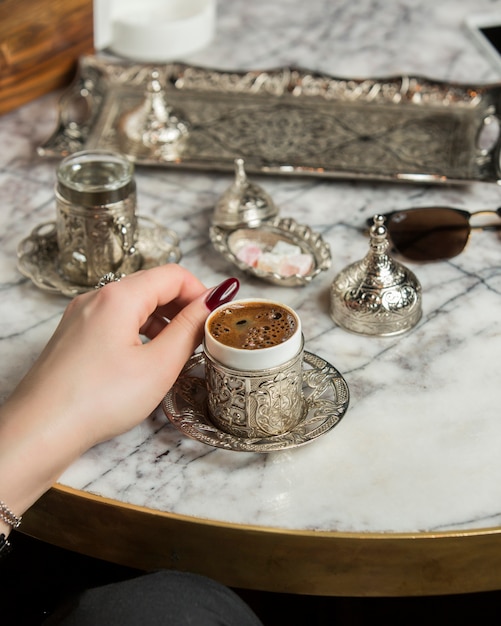 mano della donna accanto al caffè turco servito con acqua in argento turco set