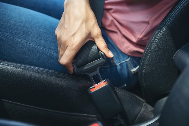 Mano della donna che allaccia una cintura di sicurezza in macchina, immagine ritagliata di una donna seduta in macchina e che indossa la cintura di sicurezza, concetto di guida sicura.