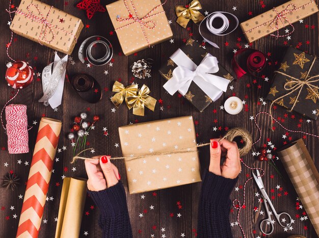Mano della donna che lega arco con spago per imballare il contenitore di regalo di Natale