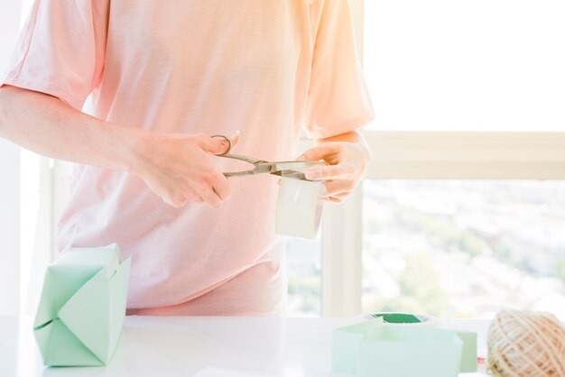 Mano della donna che taglia il nastro appiccicoso con le forbici per avvolgere il contenitore di regalo