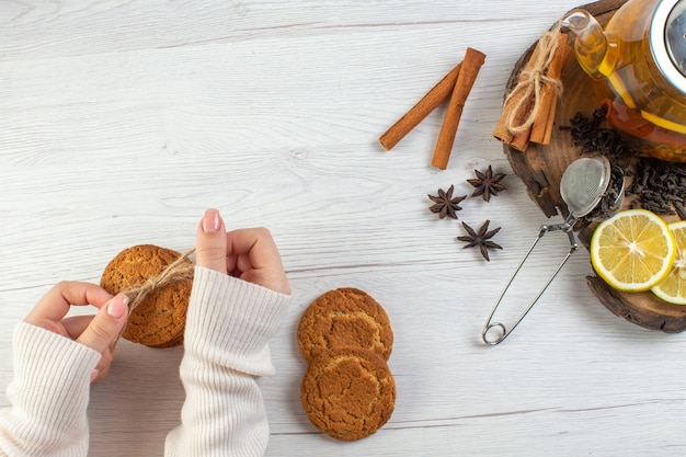 Mano della donna che tiene il tè nero impilato dei biscotti con il limone