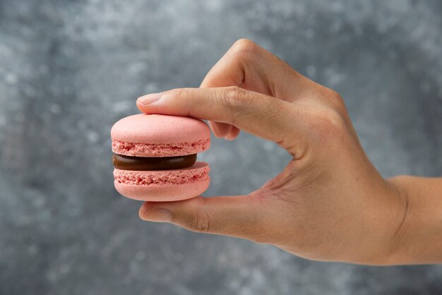 Mano della donna che tiene macaron gustoso rosa sulla superficie di marmo.