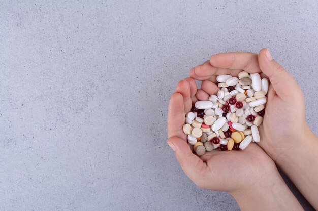 Mano della donna che tiene mucchio di pillole su fondo di marmo. Foto di alta qualità