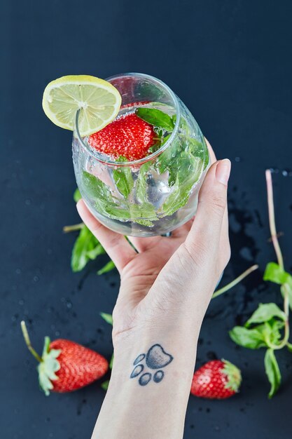 Mano della donna che tiene un bicchiere di succo con frutta intera e menta all'interno