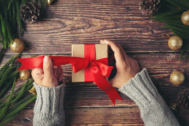 Mano della donna che tiene una confezione regalo con nastro rosso sul pavimento di legno