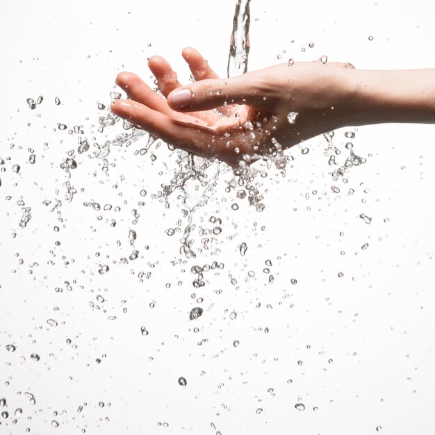 Mano della donna del primo piano sotto il flusso di spruzzi d'acqua - concetto di cura della pelle