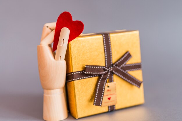 Mano di legno che tiene cuore rosso vicino a scatola regalo