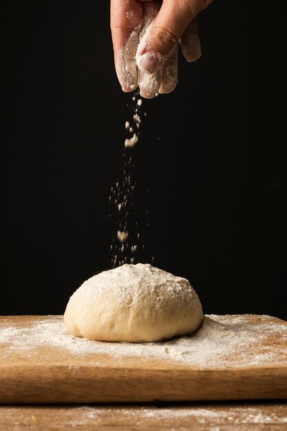 Mano di vista frontale che spruzza farina sopra pasta sul tagliere