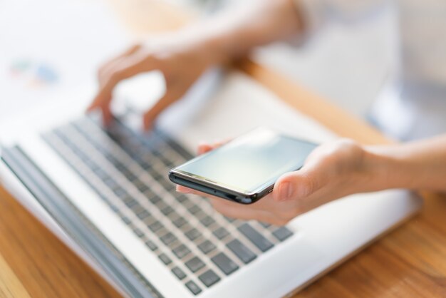 Mano donna di affari con grafici finanziari e telefono cellulare su laptop sul tavolo.