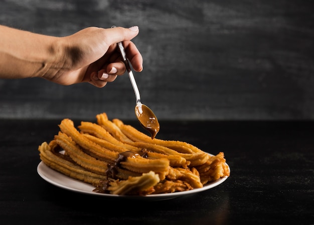 Mano e cucchiaio con deliziosi churros fritti