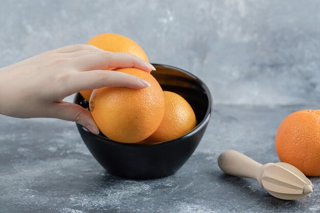 Mano femminile che prende arancia fresca dalla ciotola nera.